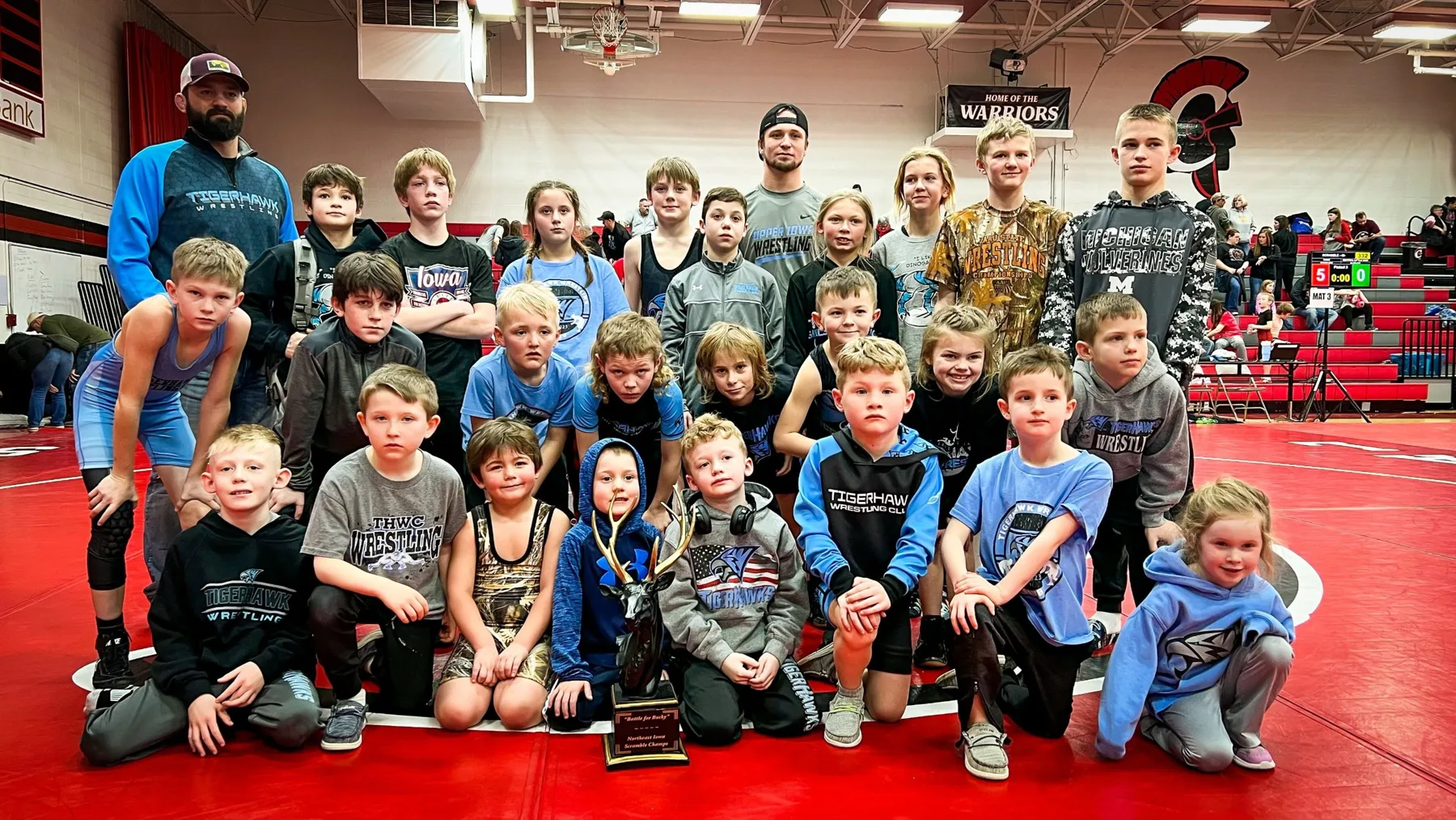 TigerHawk Wrestling Club wrestlers and coaches with the Bucky trophy on the mat in the Central gym